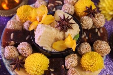 Photo of Diwali celebration. Tasty Indian sweets, anise stars and flowers on violet table