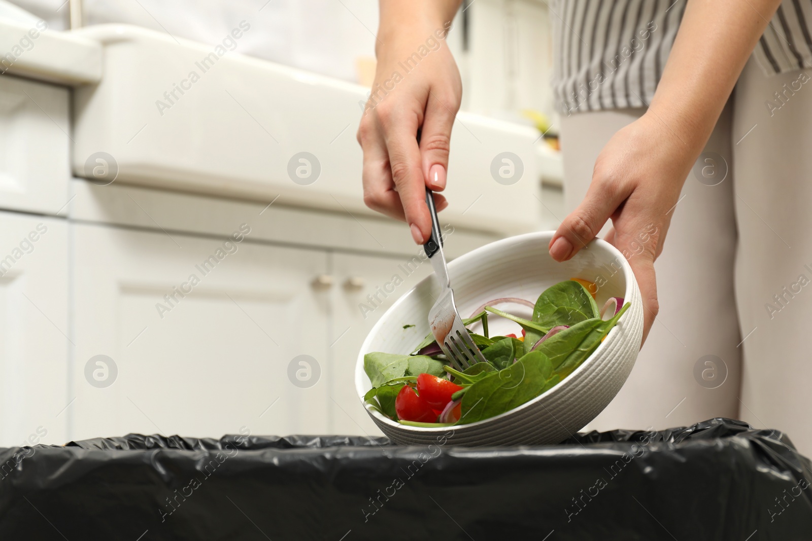 Photo of Woman throwing vegetable salad into bin indoors, closeup