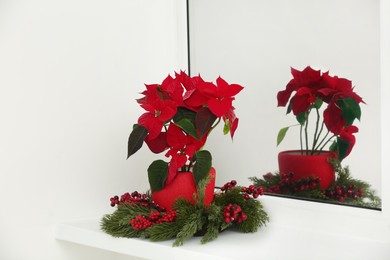 Potted poinsettia and festive decor on windowsill in room. Christmas traditional flower