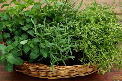 Photo of Wicker basket with fresh mint, thyme and rosemary on wooden table outdoors, closeup. Aromatic herbs