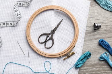 Photo of Embroidery hoop, fabric and other accessories on wooden table, flat lay