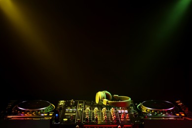 Photo of Modern DJ controller and headphones under beams of light on black background