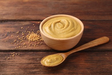 Photo of Tasty mustard sauce and dry seeds on wooden table, closeup