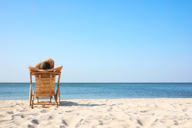 Photo of Young woman relaxing in deck chair on sandy beach