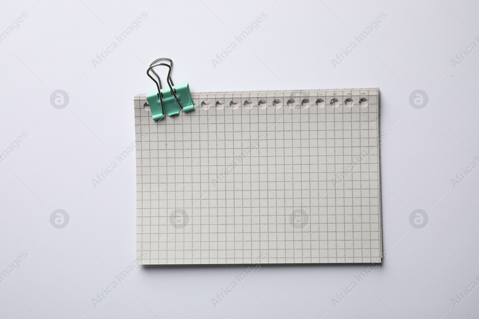 Photo of Checkered sheets of paper with binder clip on white background, top view