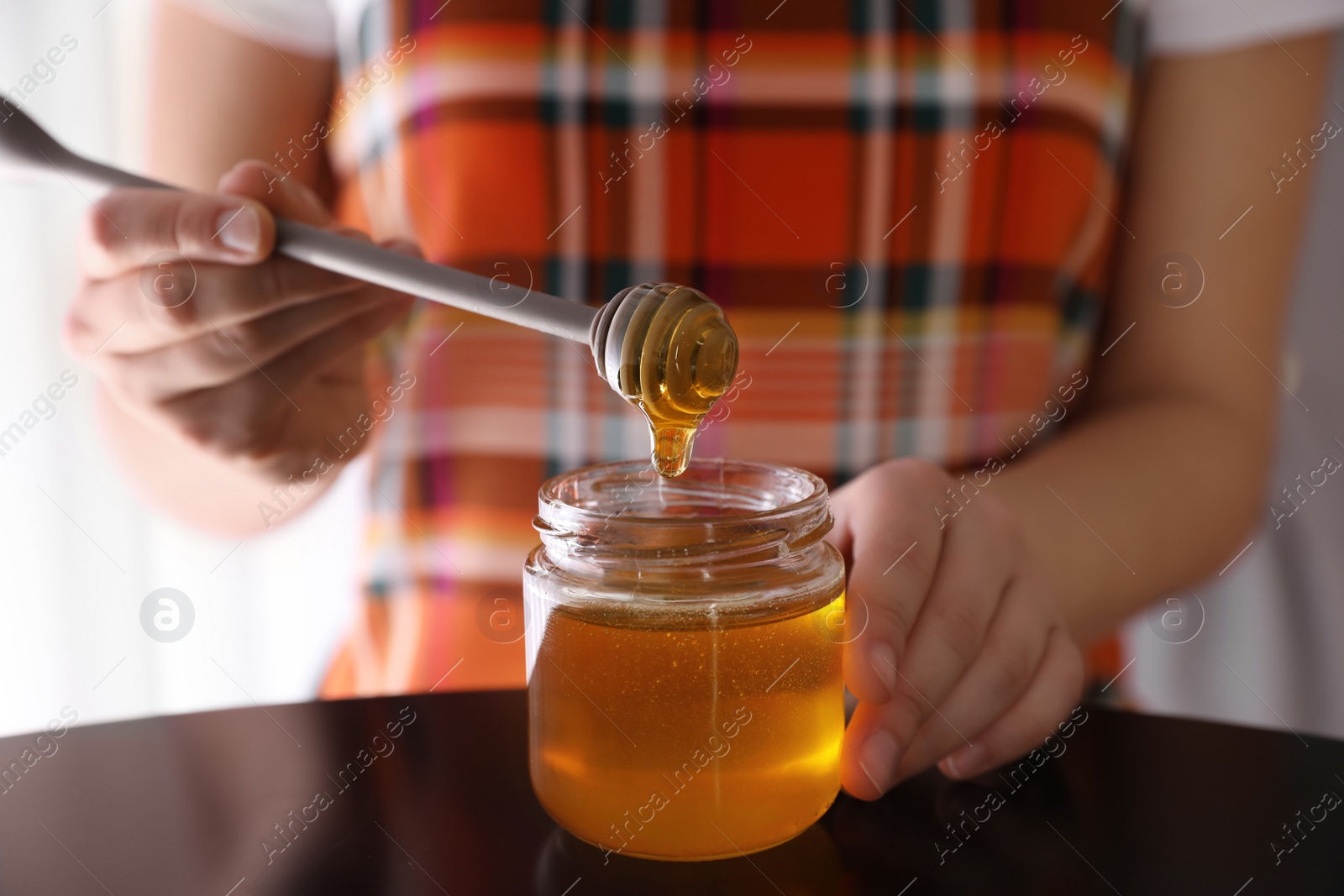 Photo of Woman with honey and dipper at black table, closeup