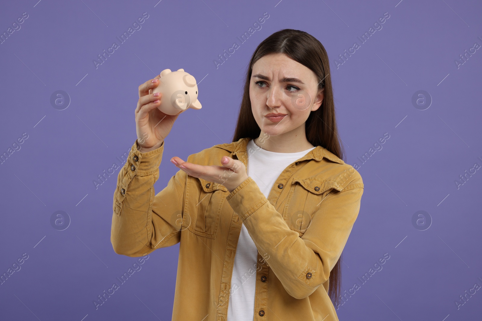 Photo of Sad woman with piggy bank on purple background