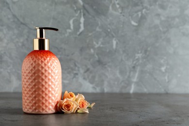 Photo of Stylish dispenser with liquid soap and beautiful flowers on grey table, space for text