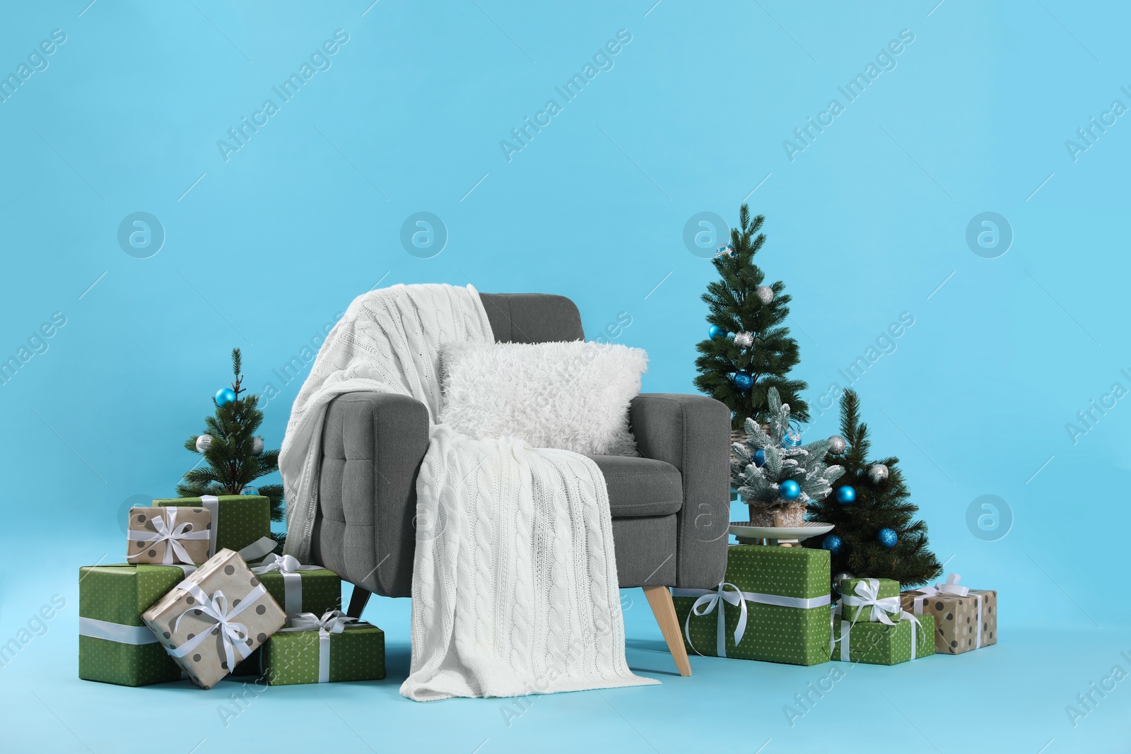 Photo of Beautiful Christmas themed photo zone with stylish armchair, trees and gift boxes on light blue background