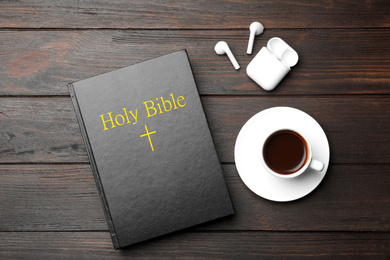 Photo of Bible, cup of coffee and earphones on wooden background, flat lay. Religious audiobook