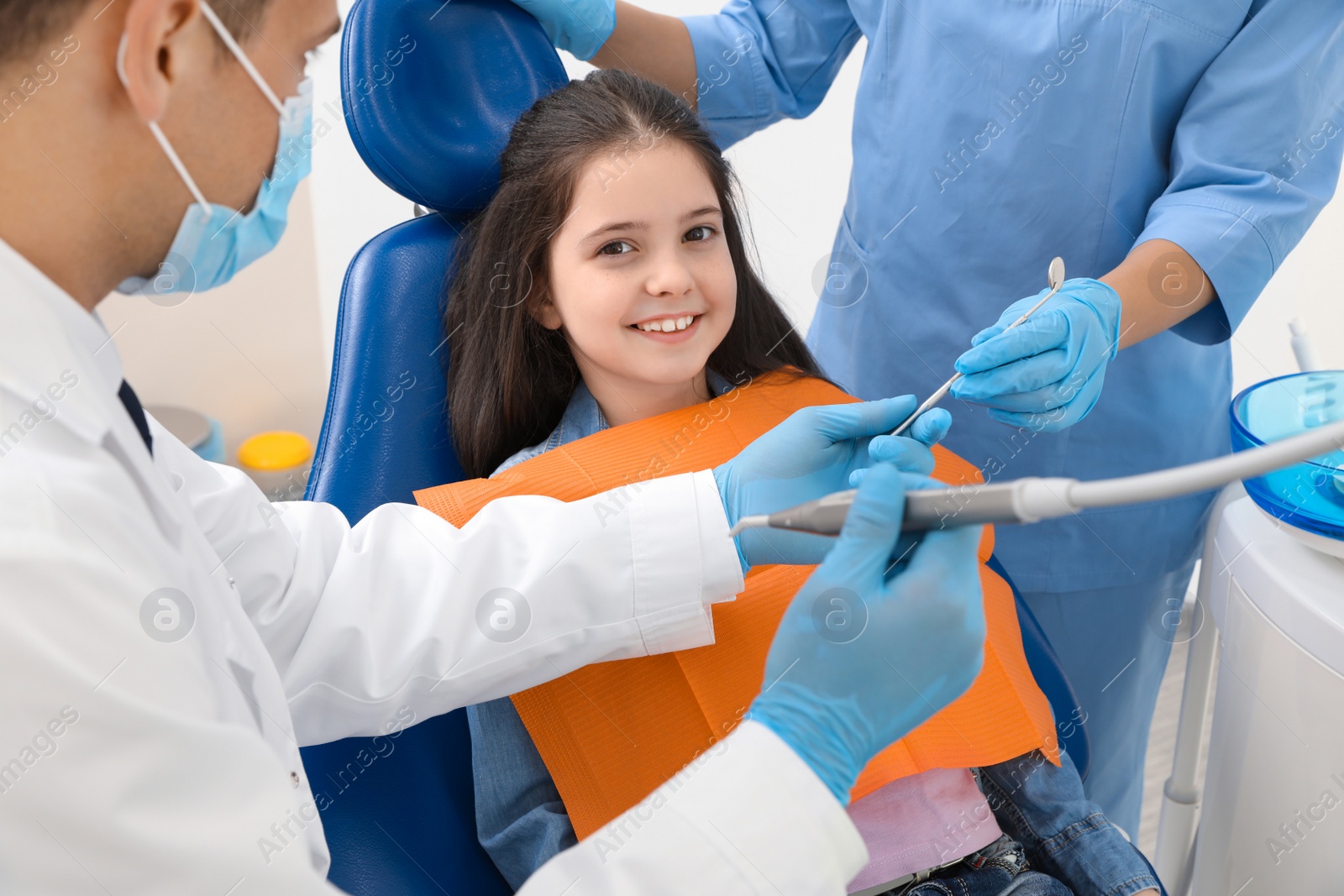 Photo of Professional dentist and assistant working with little girl in clinic