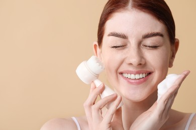 Photo of Washing face. Young woman with brush and cleansing foam on beige background, space for text