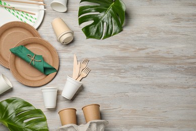 Photo of Flat lay composition with disposable tableware and monstera leaves on white wooden background. Space for text