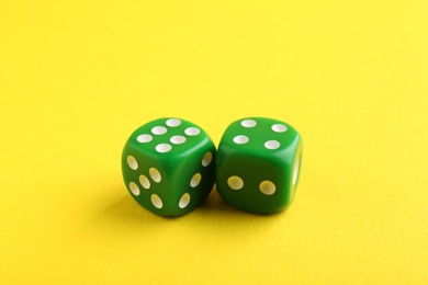 Two green game dices on yellow background, closeup