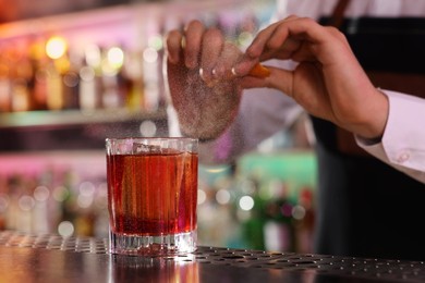 Photo of Bartender spraying orange peel onto fresh alcoholic cocktail at counter in bar, closeup