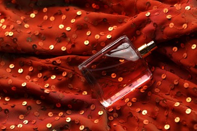 Photo of Luxury perfume in bottle on red fabric with sequins, top view