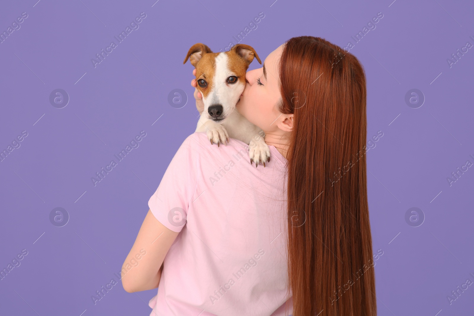 Photo of Woman kissing cute Jack Russell Terrier dog on violet background, back view