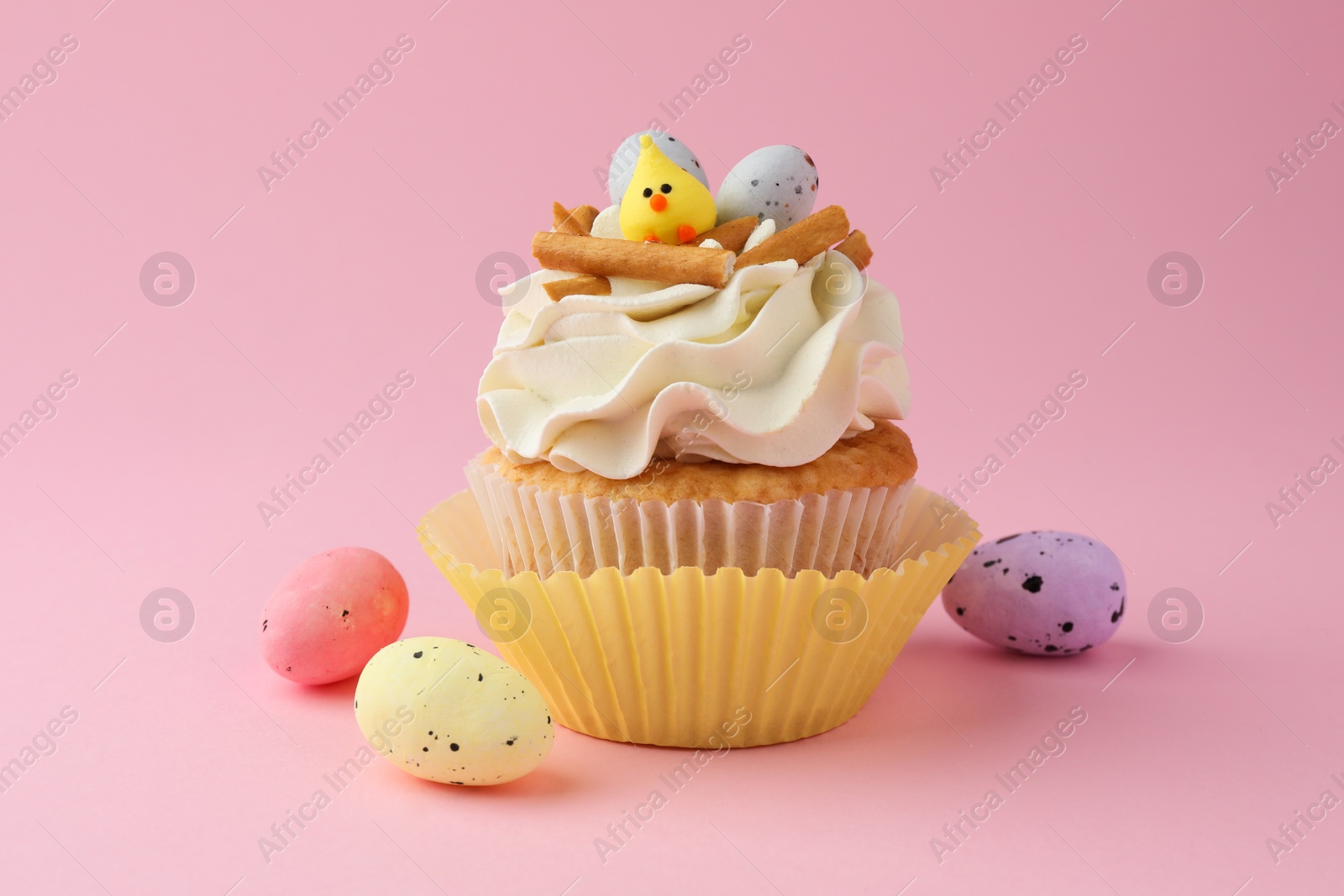 Photo of Tasty Easter cupcake with vanilla cream and candies on pink background