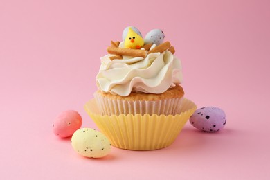 Tasty Easter cupcake with vanilla cream and candies on pink background