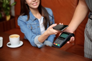 Photo of Woman using terminal for contactless payment with smartphone in cafe, closeup