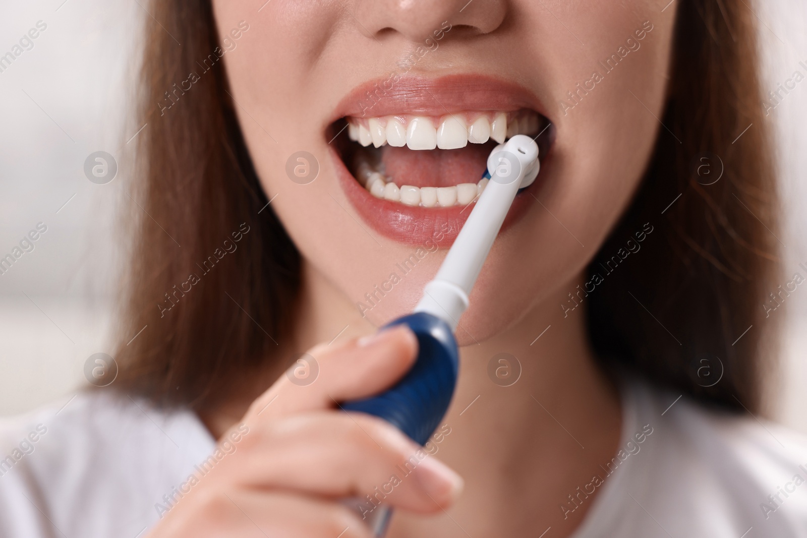 Photo of Woman brushing her teeth with electric toothbrush indoors, closeup