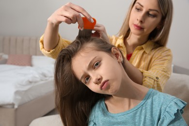 Mother using nit comb on her daughter's hair in bedroom. Anti lice treatment