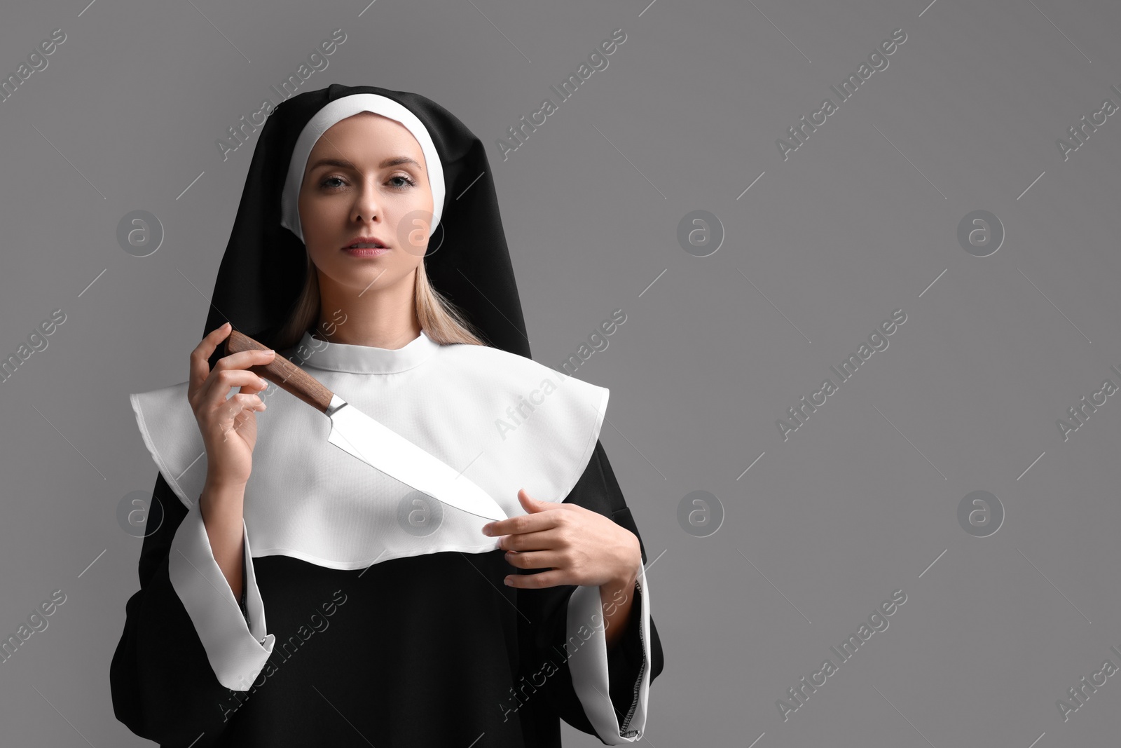 Photo of Woman in nun habit holding knife on grey background. Space for text