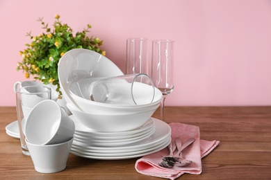 Photo of Set of clean dishes and glasses on table against color background