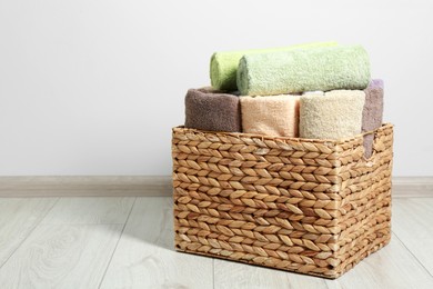 Photo of Wicker laundry basket with clean terry towels on floor indoors, space for text