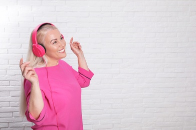 Photo of Mature woman enjoying music in headphones against brick wall. Space for text