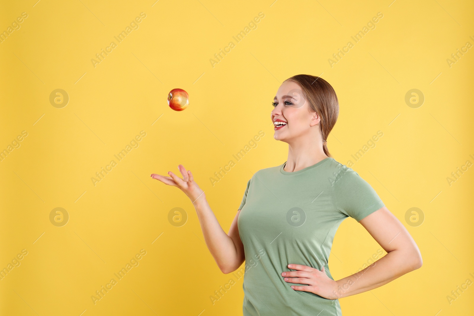 Photo of Young woman with apple on yellow background. Vitamin rich food