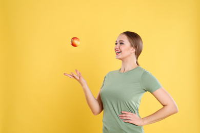 Photo of Young woman with apple on yellow background. Vitamin rich food