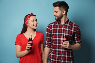 Photo of MYKOLAIV, UKRAINE - JANUARY 27, 2021: Young couple holding bottles of Coca-Cola on light blue background