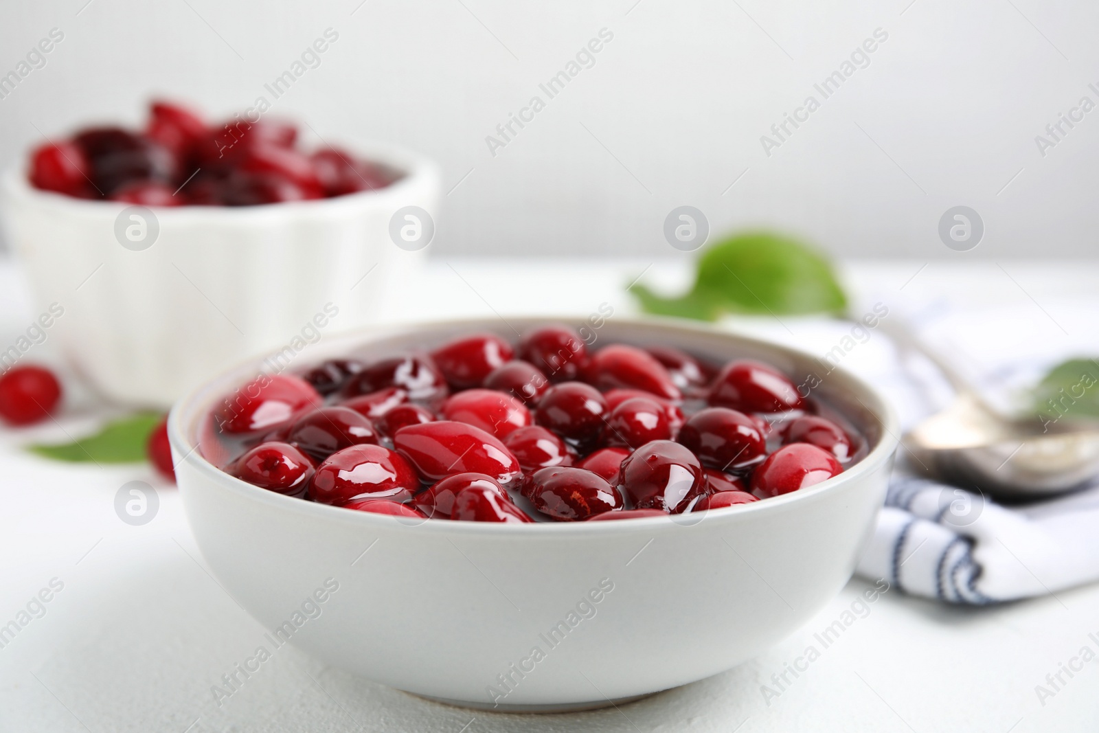 Photo of Delicious dogwood jam with berries in bowl on white table, closeup