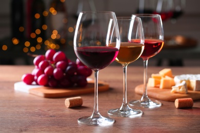 Glasses with different wines and appetizers on wooden table against blurred background. Space for text