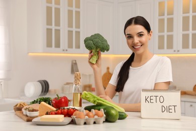 Happy woman near notebook with words Keto Diet and different products in kitchen