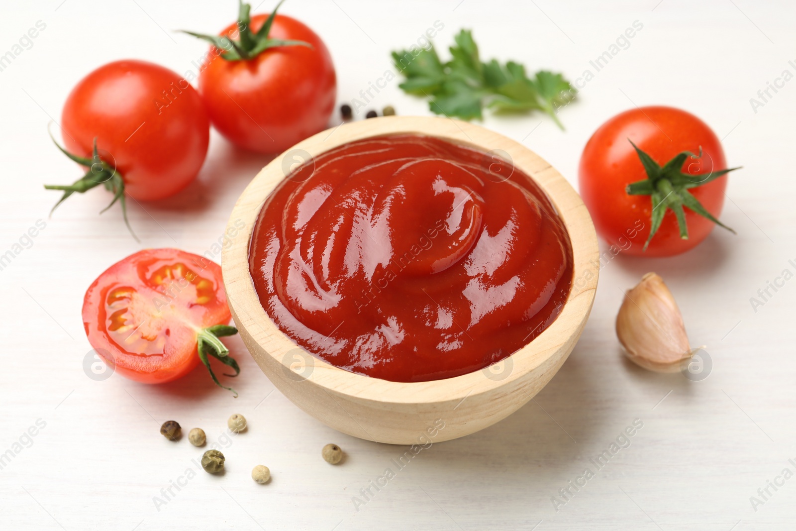 Photo of Delicious ketchup in bowl, garlic and tomatoes on white wooden table, closeup