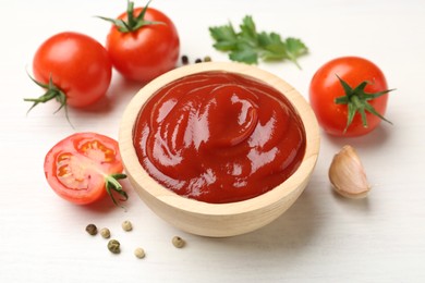 Photo of Delicious ketchup in bowl, garlic and tomatoes on white wooden table, closeup