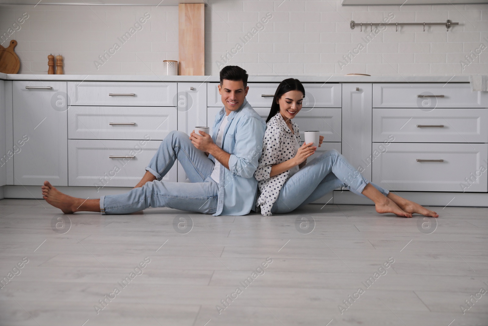 Photo of Happy couple sitting on warm floor in kitchen. Heating system