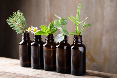 Photo of Glass bottles of different essential oils with plants on table