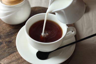 Photo of Pouring milk into cup with tea on light table, closeup