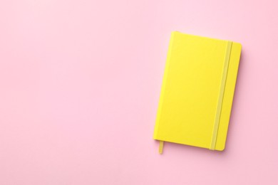 Photo of Closed yellow notebook on light pink background, top view. Space for text