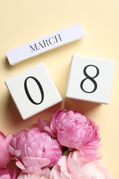 Photo of International Women's day - 8th of March. Wooden block calendar and beautiful flowers on beige background, flat lay