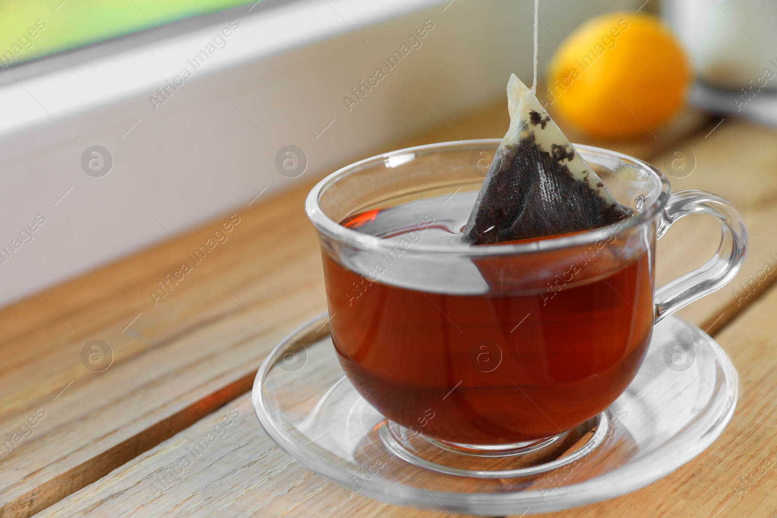 Photo of Bag of black tea in cup with hot water on wooden table indoors