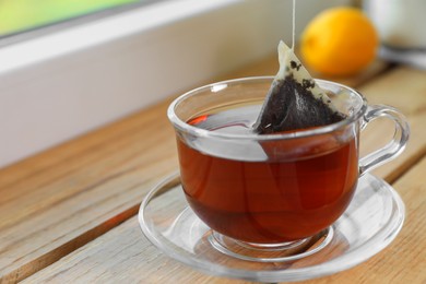 Bag of black tea in cup with hot water on wooden table indoors