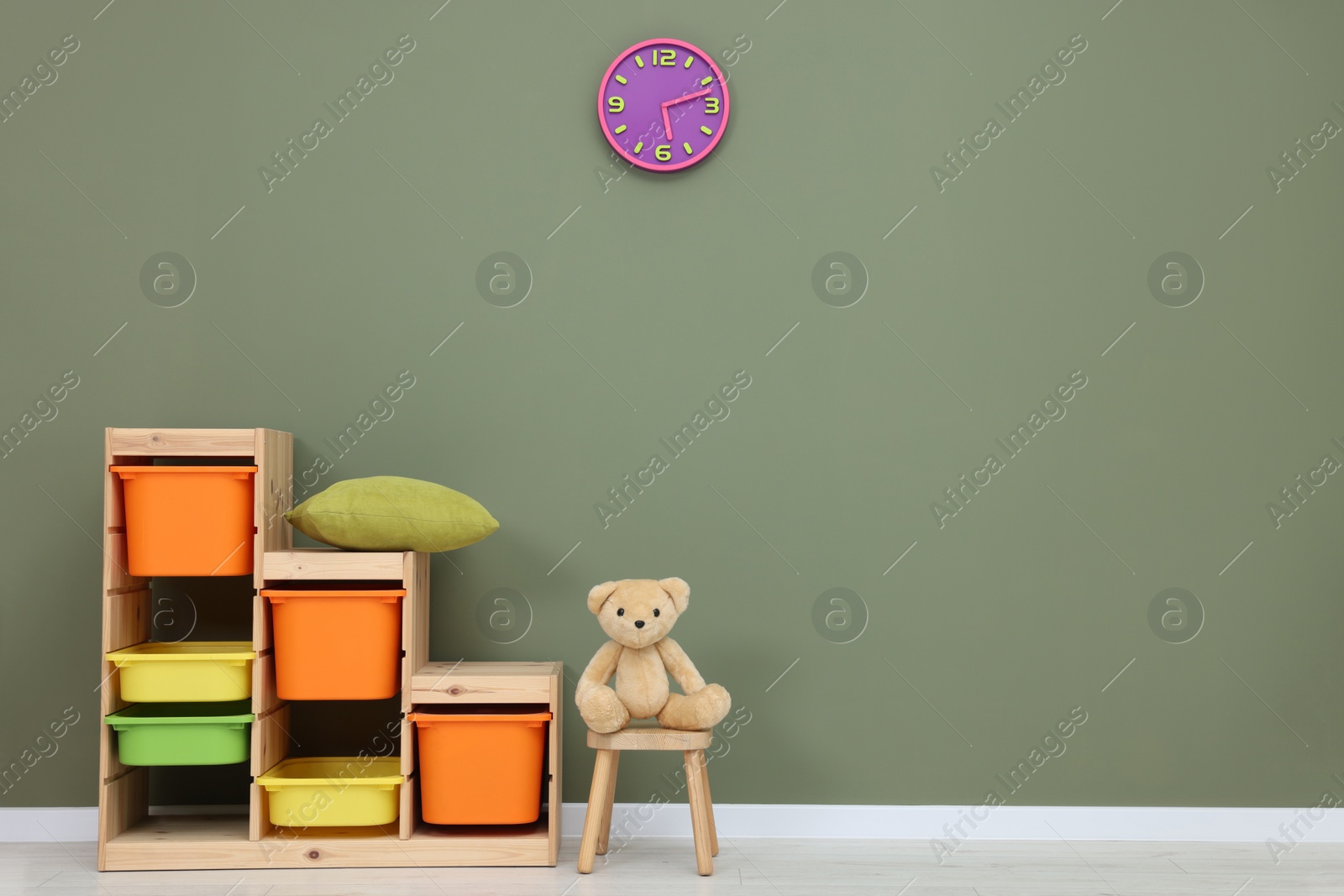 Photo of Shelves and teddy bear on chair near olive wall in playroom, space for text. Stylish kindergarten interior