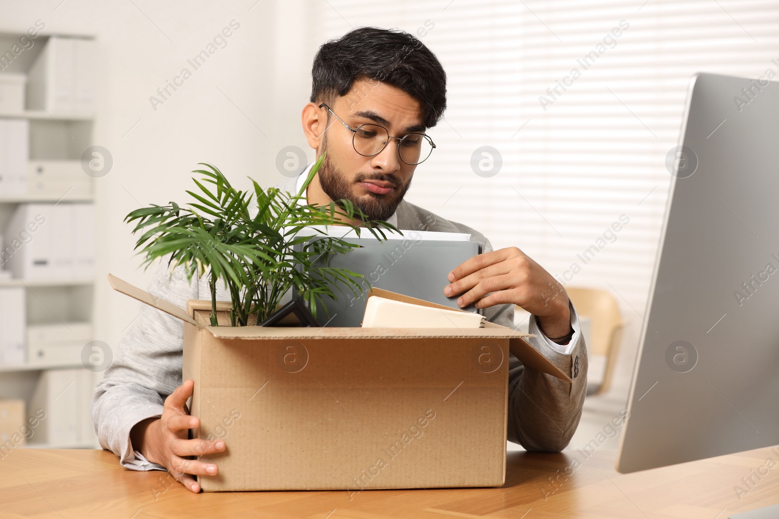 Photo of Unemployment problem. Frustrated man with box of personal belongings at desk in office