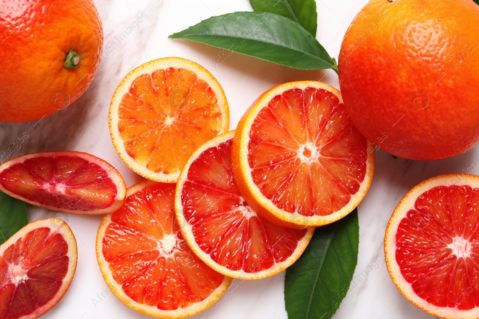 Photo of Whole and cut red oranges with green leaves on white marble table