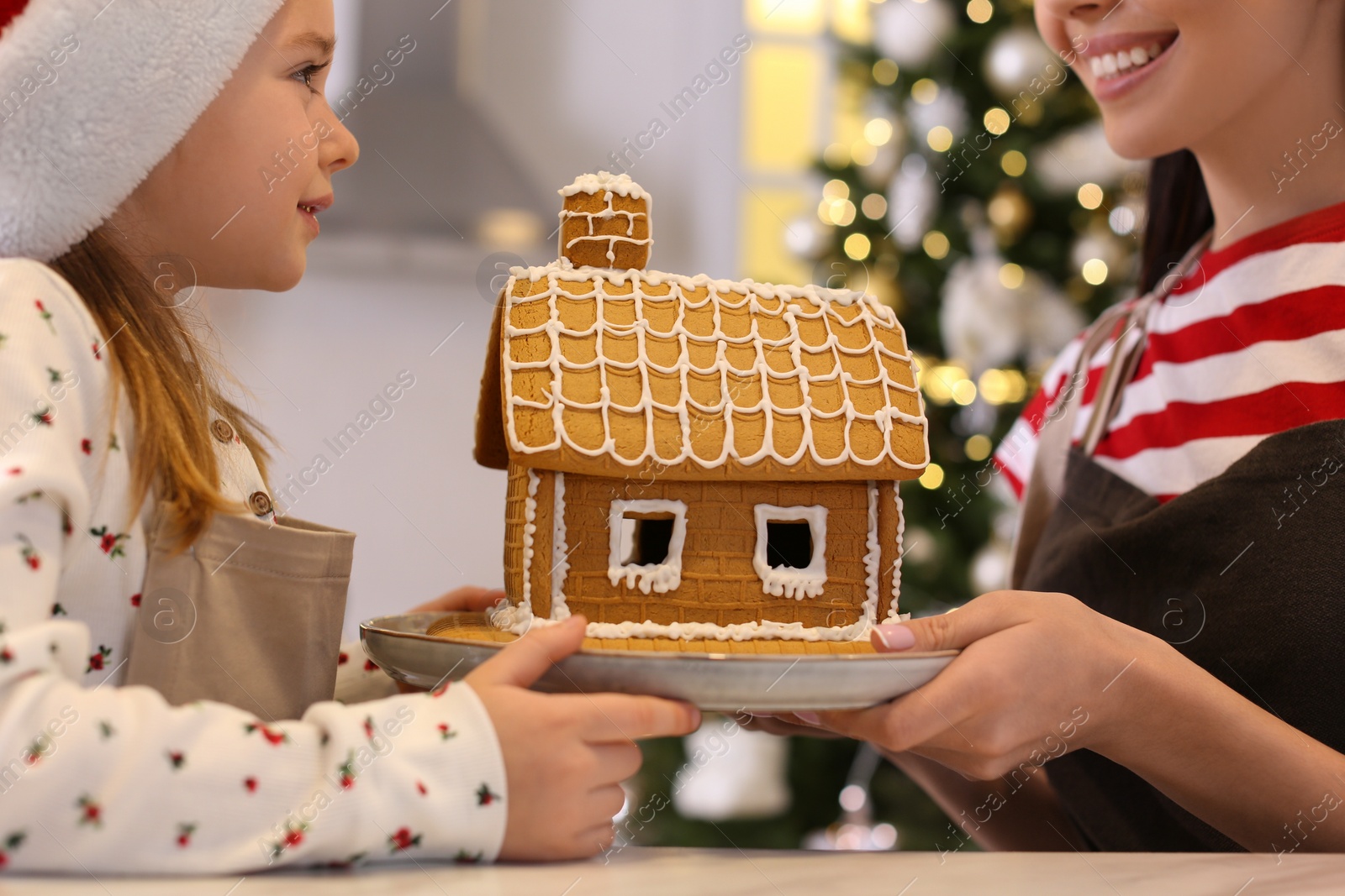 Photo of Mother and daughter with gingerbread house in kitchen, closeup