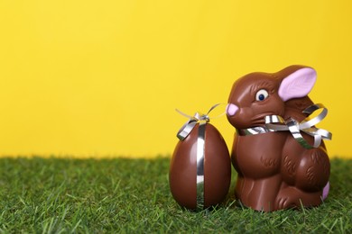 Photo of Easter celebration. Cute chocolate bunny and egg on grass against yellow background, space for text
